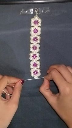 two hands are working on a beaded bracelet with pearls and pink flowers in the middle