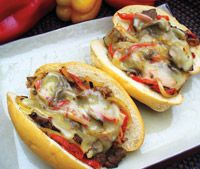 two hot dogs with toppings sit on a tray next to some peppers and tomatoes