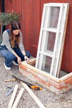 a woman kneeling down next to an old window with tools around her on the ground