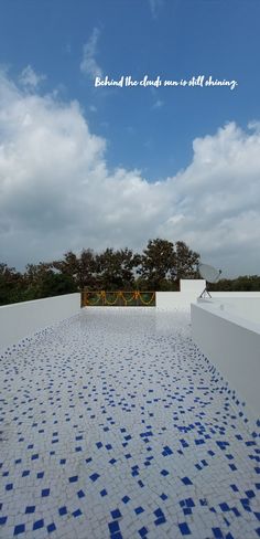 an empty swimming pool with blue and white tiles on the ground, under a cloudy sky