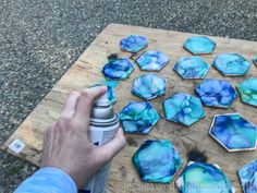 someone is painting blue and green marbles on a wooden cutting board with spray paint