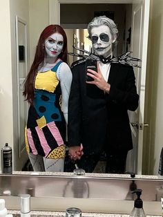 two people dressed up in halloween costumes standing in front of a bathroom mirror with makeup on