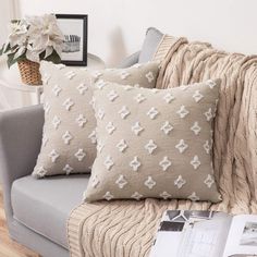 a couch with two pillows on top of it next to a book and flower vase