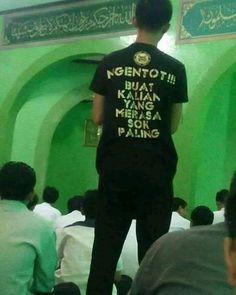 a man standing in front of a green wall wearing a t - shirt with words on it