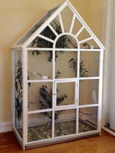 a small white bird cage sitting on top of a hard wood floor next to a wall