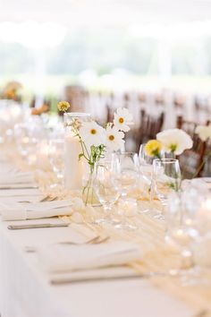 the table is set with white and yellow flowers in vases, wine glasses, and napkins