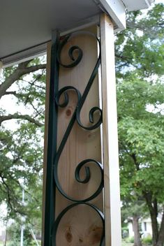 a close up of a wooden sign with iron work on it's side and trees in the background