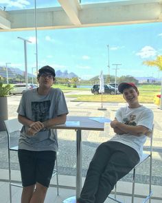 two young men sitting at a table in front of a glass wall with the sun shining on them