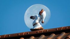 a teddy bear sitting on top of a roof with the moon in the background