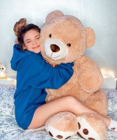 a woman hugging a large teddy bear on top of a bed