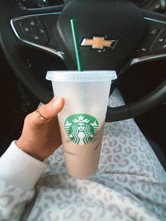 a person holding a starbucks cup in their hand while sitting in a car with the steering wheel behind them