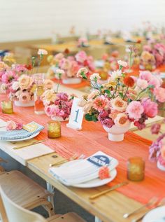 the table is set with orange and pink flowers, greenery, and wine glasses