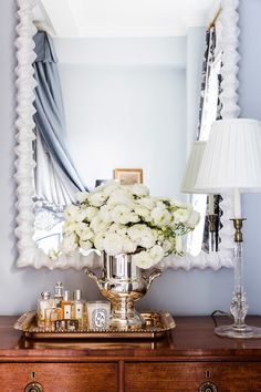 a mirror sitting on top of a dresser next to a vase filled with white flowers