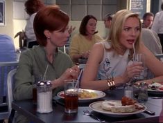 two women sitting at a table with plates of food and drinks in front of them