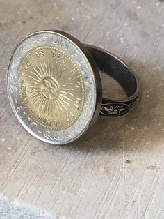 Coin ring.  It was made with a real  coin featuring the face of the sun.  The ring is finely tooled and it is adjustable to a size 10.  The adjustable section is underneath the token so that it looks just like a solid ring.  No one can see the difference. The coin is gold tone and the band is silver. Southport Nc, Coin Ring, Coin Jewelry, The Band, Adjustable Ring, Adjustable Rings, The Face, The Sun, Gold Tones