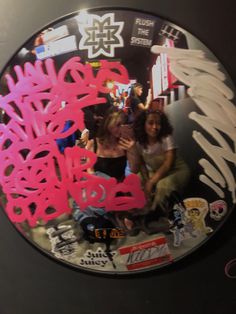 two women are sitting in front of a clock with pink graffiti on the face and hands