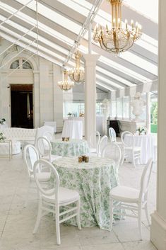 a dining room with tables and chairs covered in white tablecloths, chandeliers and windows