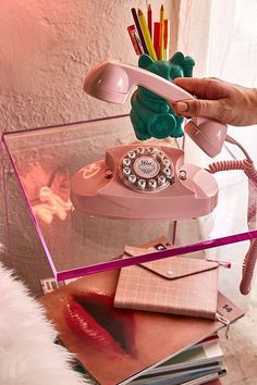 a pink telephone sitting on top of a glass table next to books and pencils