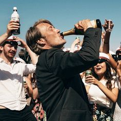 a man drinking from a beer bottle while surrounded by people