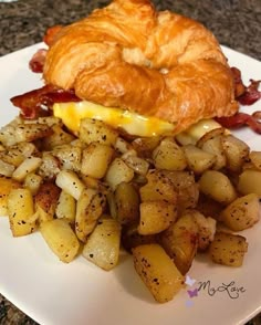 a breakfast sandwich with potatoes and bacon on a white plate next to a croissant