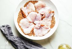 a white bowl filled with meat and spices next to a glass of wine on a table