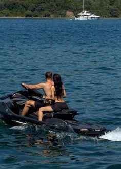 a man and woman riding on the back of a black jet ski in the ocean