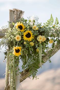 a bouquet of sunflowers and greenery on a wooden cross