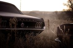 an old car parked in the middle of a field with tall grass and weeds around it