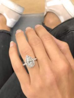 a woman's hand with a diamond ring on her finger and white shoes in the background