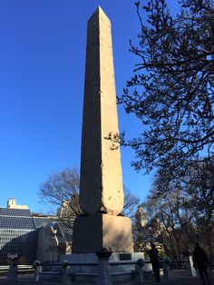 a tall obelisk in the middle of a park with people walking around it