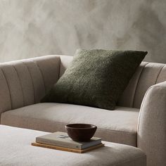 a couch with a wooden bowl on top of it next to a book and pillow