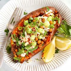 a white plate topped with a stuffed sweet potato covered in vegetables and garnish