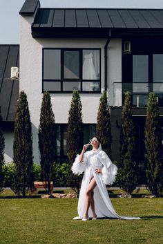 a woman standing in front of a house wearing a white dress and feathered cape