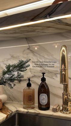 a bathroom sink with soap and lotion bottles on top of it next to a gold faucet