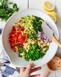 a white bowl filled with pasta, peas and carrots next to lemon wedges