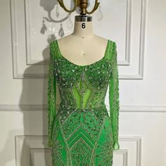 green beaded dress on display in front of white wall with door and light fixture