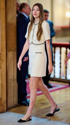 a woman in a short white dress is walking down the hall with her hand on her hip