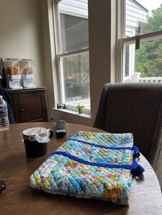 a quilted table runner sitting on top of a wooden table next to a window