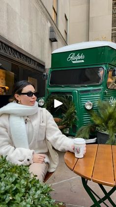 a woman sitting at a table in front of a green bus