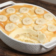 a banana pudding in a white dish on top of a wooden table with sliced bananas