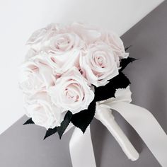 a bridal bouquet with white roses and black leaves is on the grey wall behind it