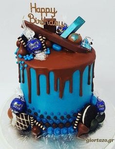 a blue and brown birthday cake on a white plate with chocolate icing, candies and candy