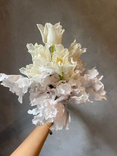 a bouquet of white flowers is held by a woman's hand in front of a gray wall