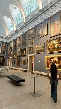 a woman is looking at paintings on display in an art museum with vaulted ceiling and high ceilings