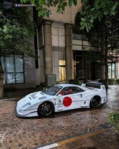 a white sports car parked in front of a building on a brick street with trees