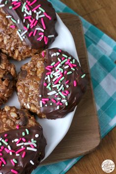 chocolate covered cookies with colorful sprinkles on a white plate next to a blue checkered napkin