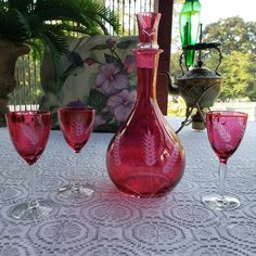 three wine glasses and a decanter are sitting on a table with a floral pillow in the background