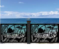 an iron gate with sea scene and fish on it in front of the ocean under a partly cloudy blue sky