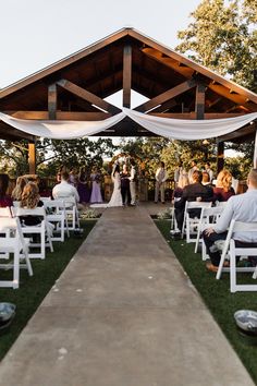 an outdoor wedding ceremony with white chairs and people sitting on the grass at the end of the aisle