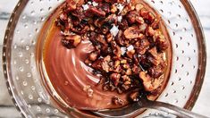 a bowl filled with chocolate and nuts on top of a marble countertop next to a spoon